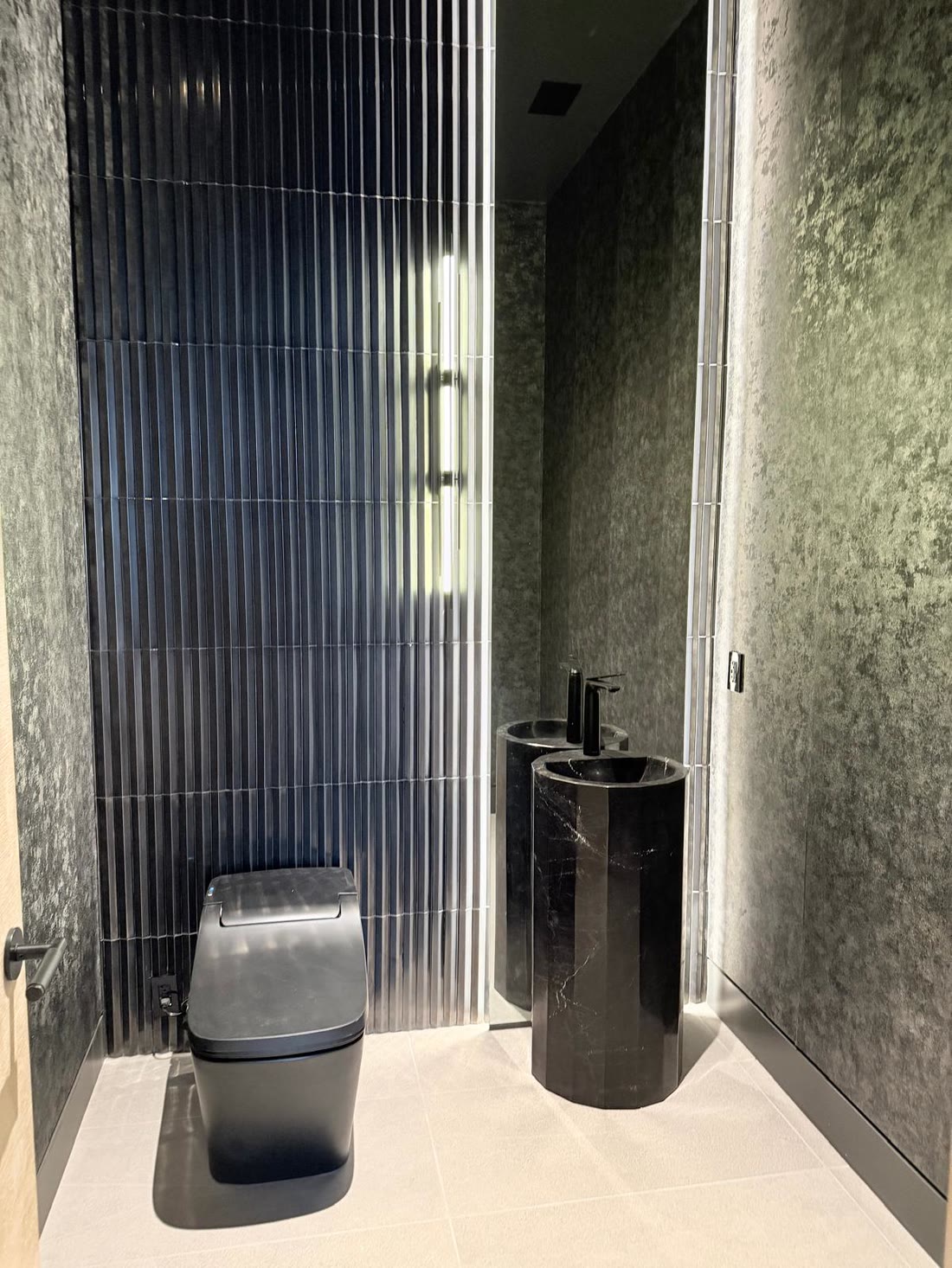 The powder room: fluted black tile, a black marble pedestal basin and mottled dark walls