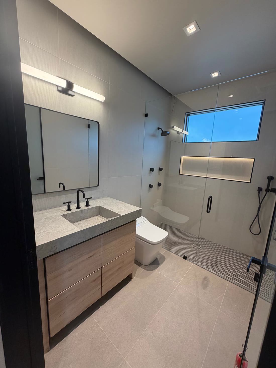 A guest bathroom with a lit shower niche and a penny tile shower floor