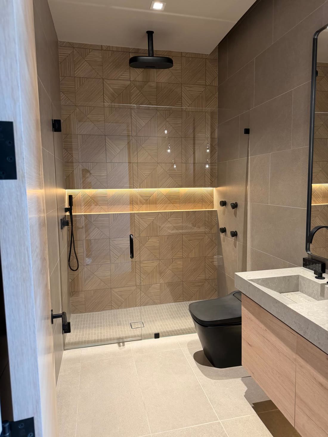 A shower lined in geometric timber effect tile with a lit horizontal niche