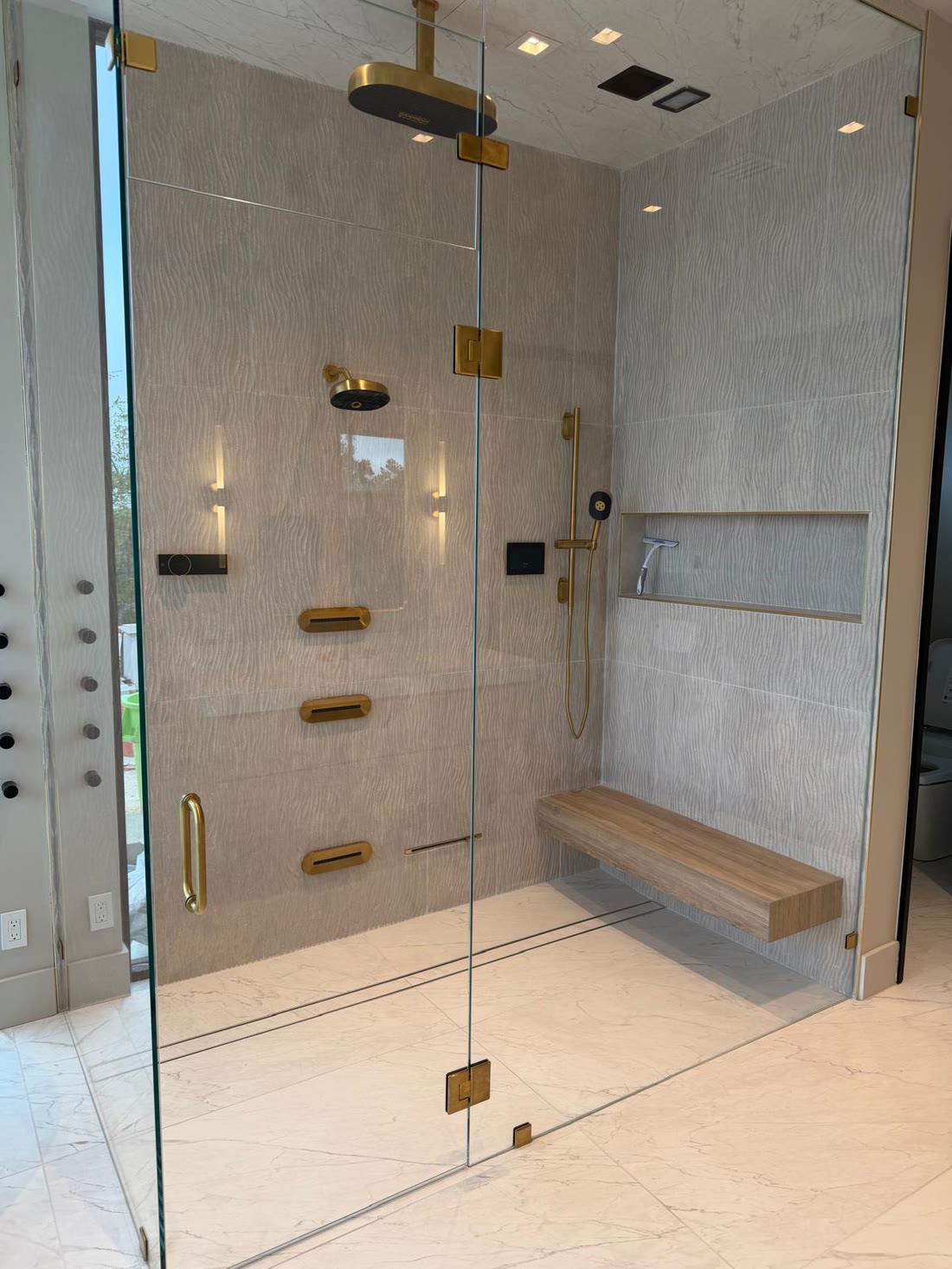 The principal shower in textured stone with brushed brass fittings and a timber bench