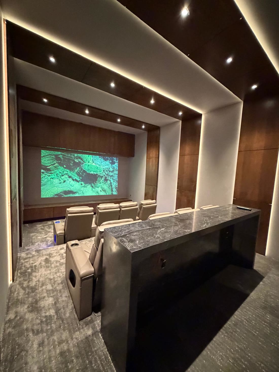 The screening room with tiered leather seating, timber panelling and a stone bar counter