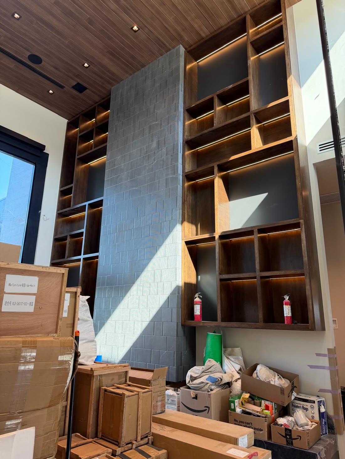 The double height bookwall in walnut with lit shelves either side of a stone chimney
