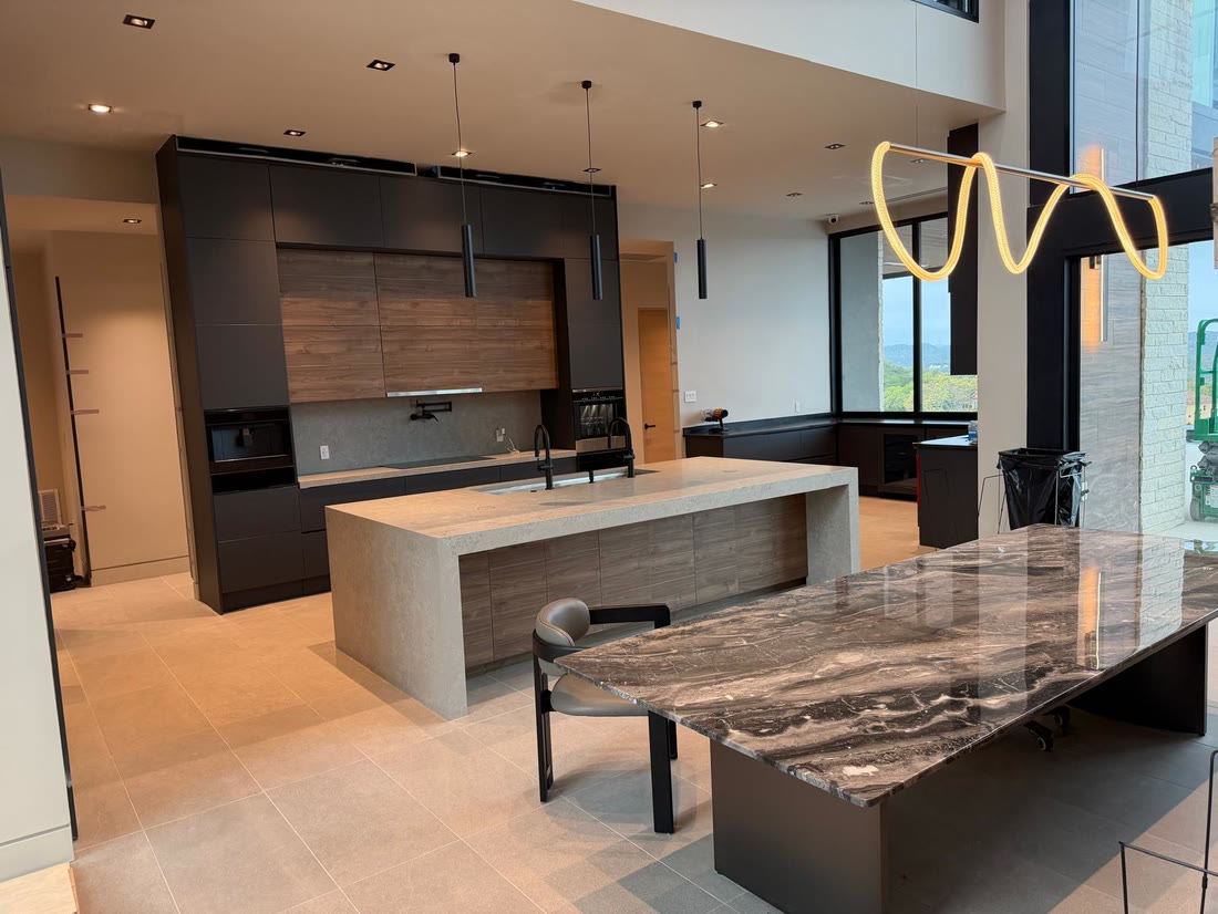 The finished kitchen: graphite cabinetry, a walnut hood surround, a pale quartzite island and a figured granite table under a looping light