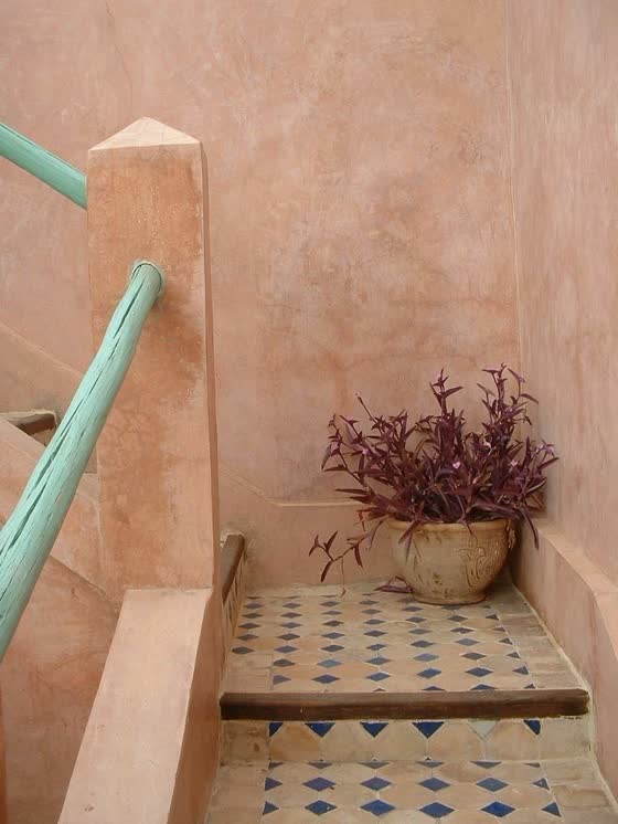 A pink limewash stairwell with a mint painted handrail and patterned floor tile