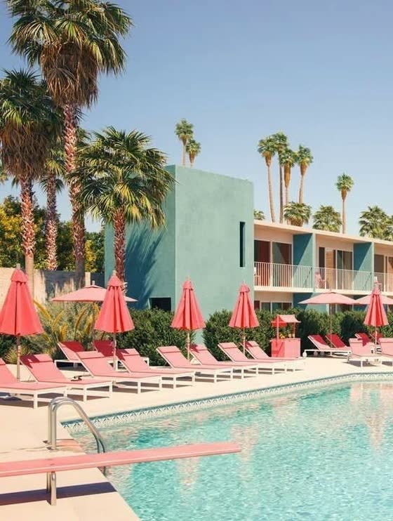 A Palm Springs motel pool with coral loungers, umbrellas and a mint green block