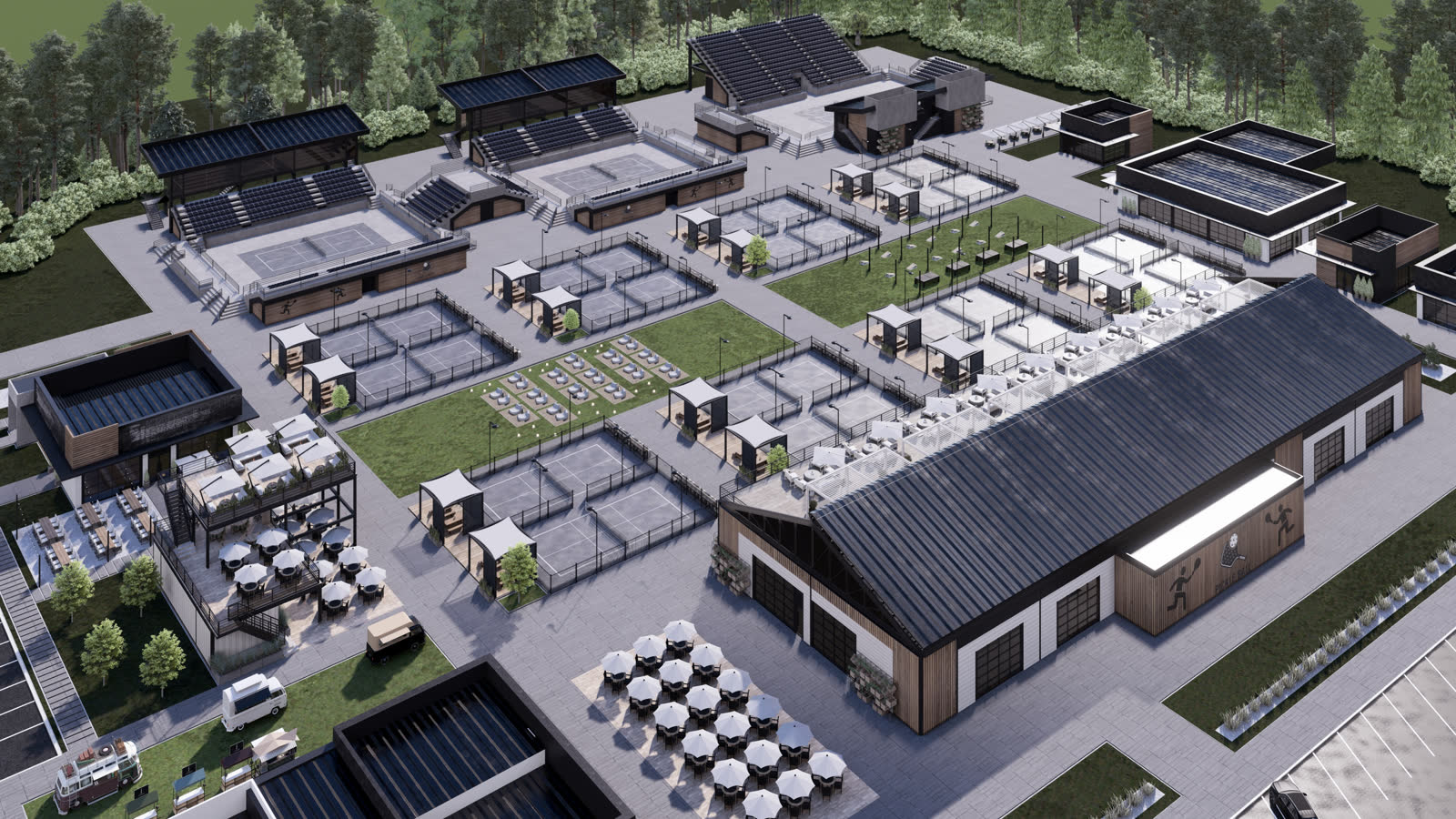 The pickleball club from the air: the indoor court hall with its dark roof, rows of fenced outdoor courts, the food hall and rooftop bar, and the lawn between them, ringed by pines